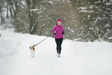 Woman jogging in the snow with her dog on a leash