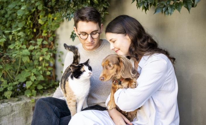 Young couple sitting in backyard holding a cat and a dog