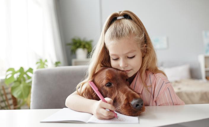 Little Girl Embracing Dog doing Schoolwork