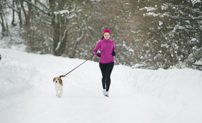 Woman jogging in the snow with her dog on a leash